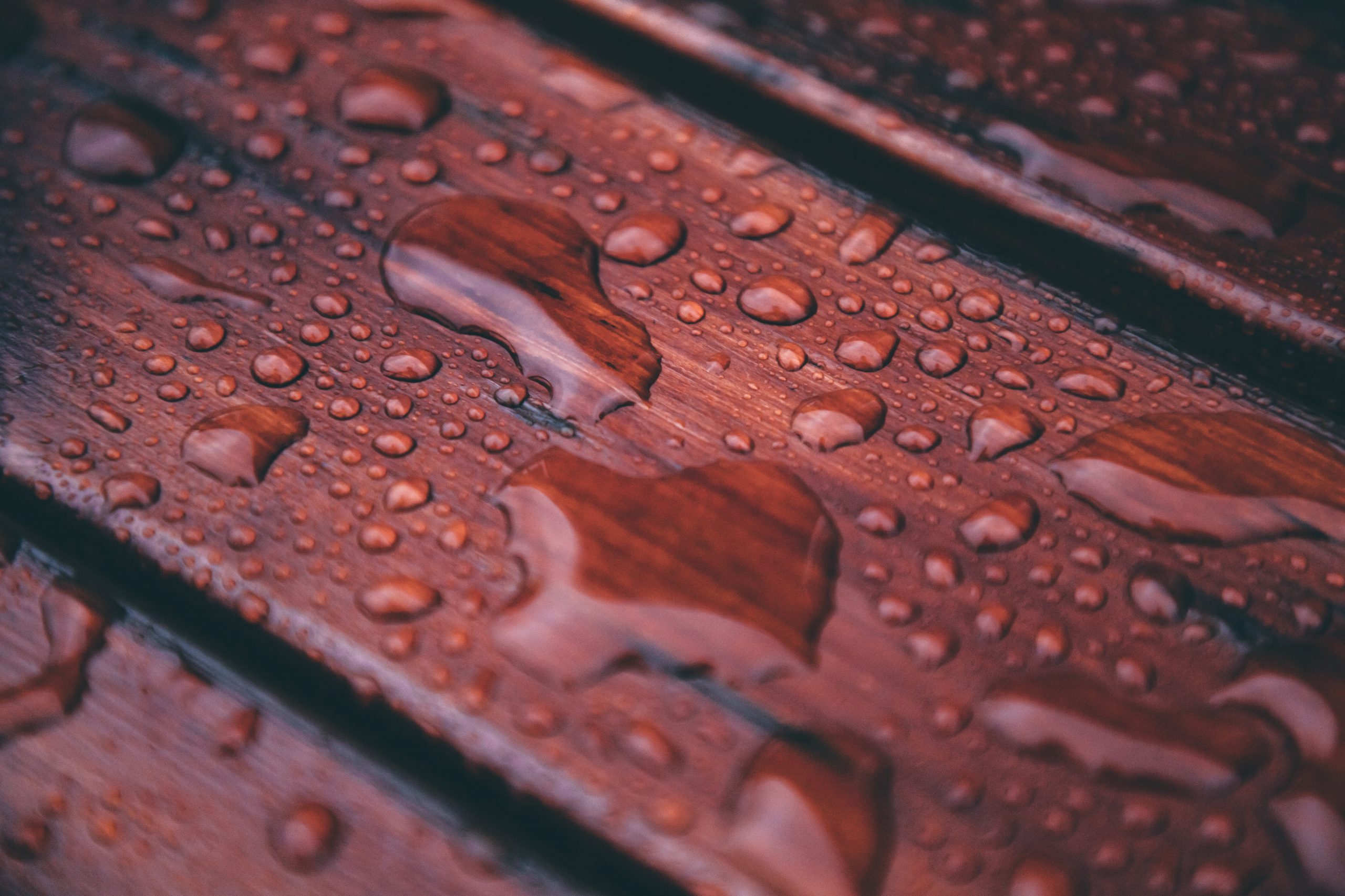 Rain drops collect on brownish red wood